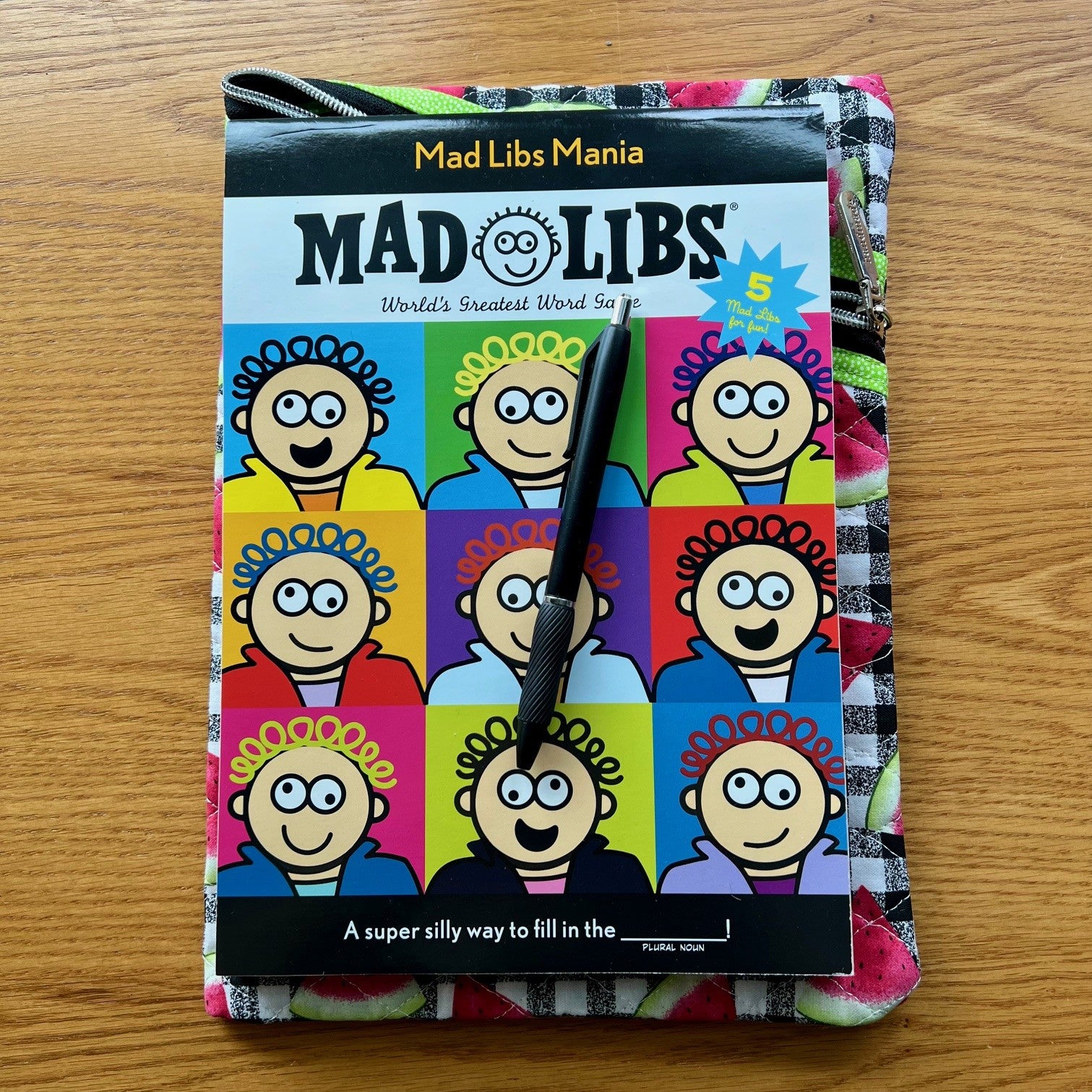 Quilted zipper pouch with a large book and pen on top of it to show sizing.