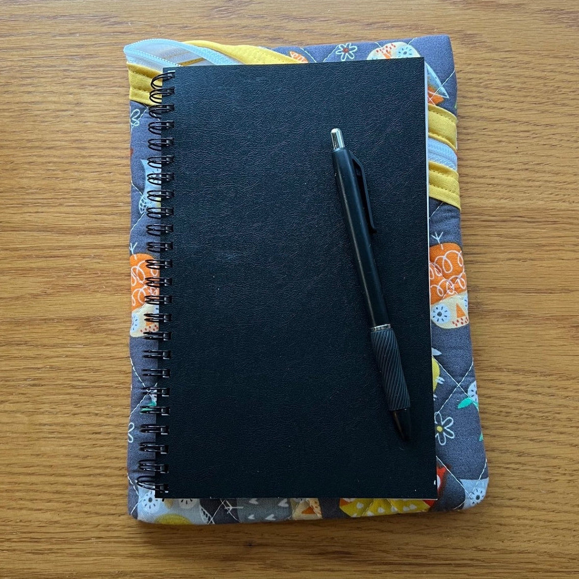 Quilted zipper pouch with a journal and pen on top of it to show sizing.