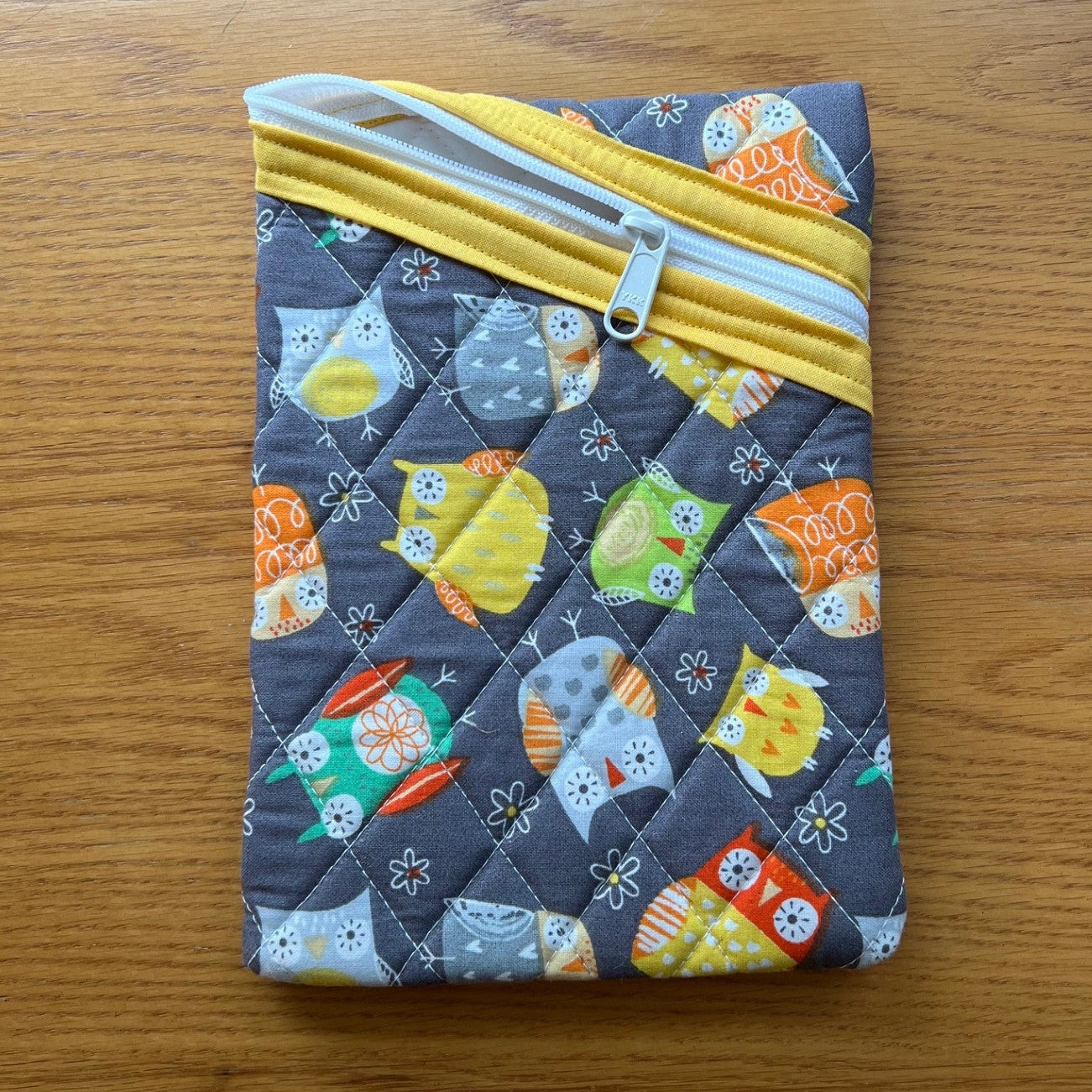 Zipper pouch with a quilted grey fabric featuring a colorful owl print.